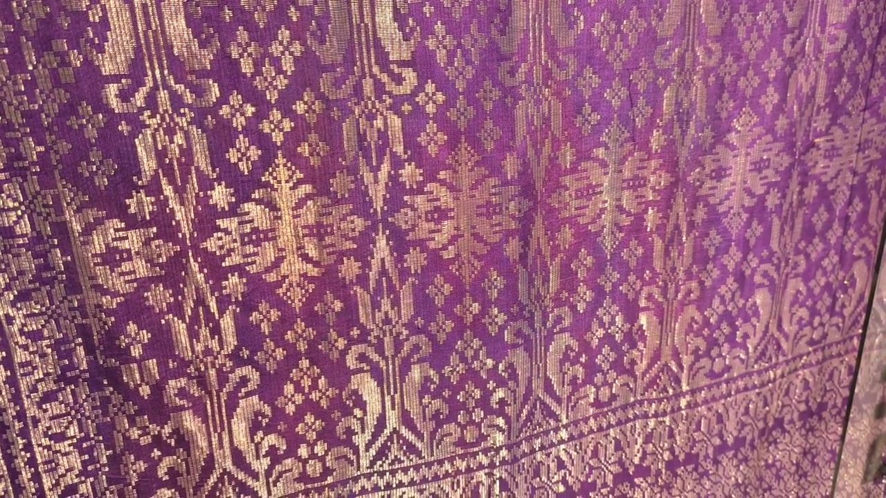 Primo piano dettagliato di lussuoso tessuto Songket. L'intricato ricamo dorato brilla sulla superficie tessuta a mano. Questo prestigioso tessuto malese è riservato alle occasioni più speciali.