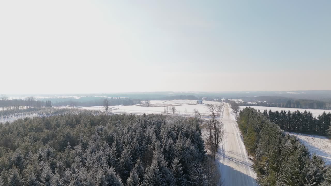 Crane drone shot of snowy sideroad and forest in Caledon, Ontario, Canada