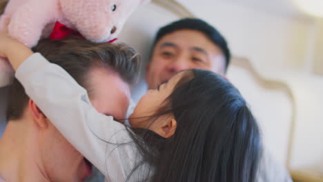 family with two dads in bed at home playing game with daughter and her soft toy