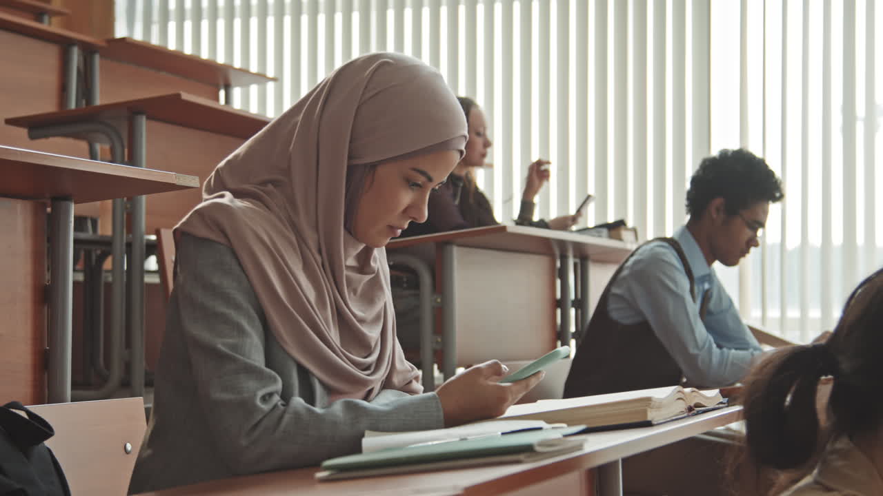 Pelajar Muslim Perempuan Duduk di Meja Menggunakan Smartphone