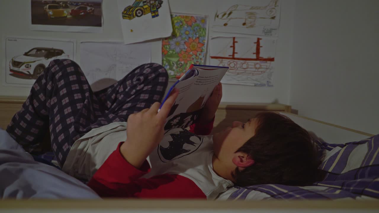 Side view of caucasian boy reading a fairytale lying on his bed before sleep, Medium 4K shot