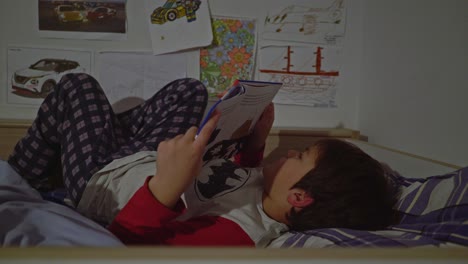 vista lateral de un niño caucásico leyendo un cuento de hadas acostado en su cama antes de dormir, toma media de 4k