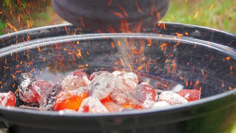 blazing hot coal stored in chimney container being poured into the bowl shaped grill. food preparation and outdoors activity concept.