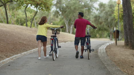 long shot of caucasian couple walking with bicycles in summer