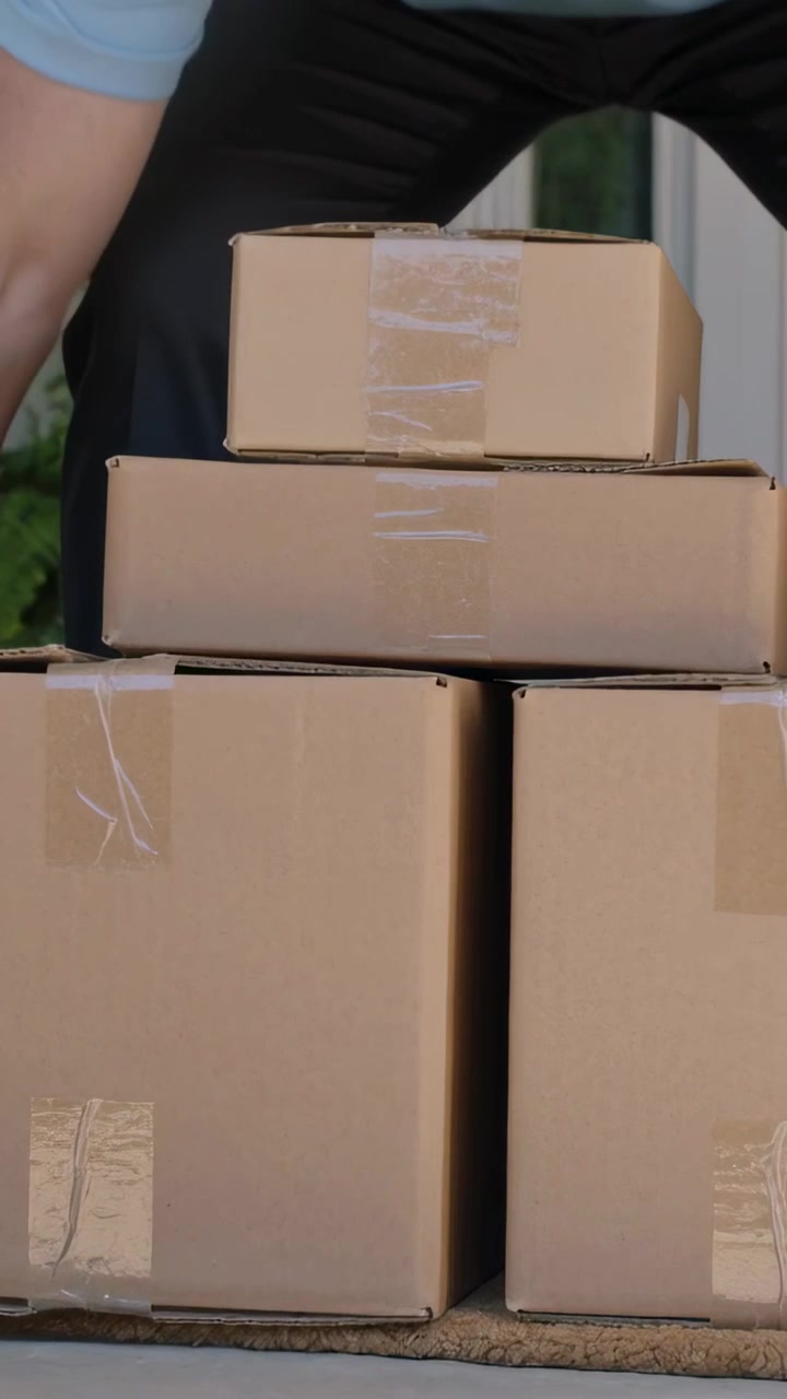 Vertical video: Stepping onto doormat, courier in polo placing four parcels at porch to deliver