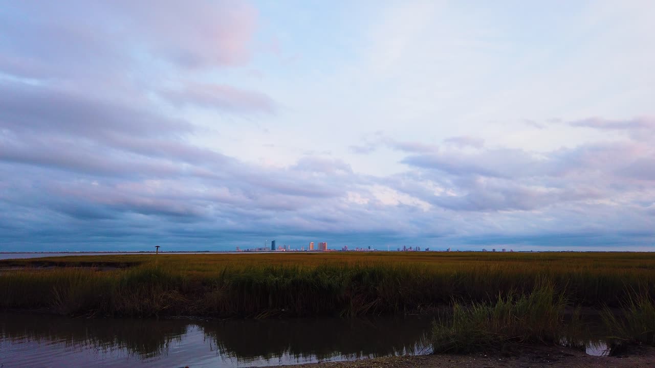4k timelapse horizonte de la ciudad atlántica en la distancia sobre la vía fluvial con cielo en su mayoría nublado de día a noche con nubes que se vuelven rosas, púrpuras y azules