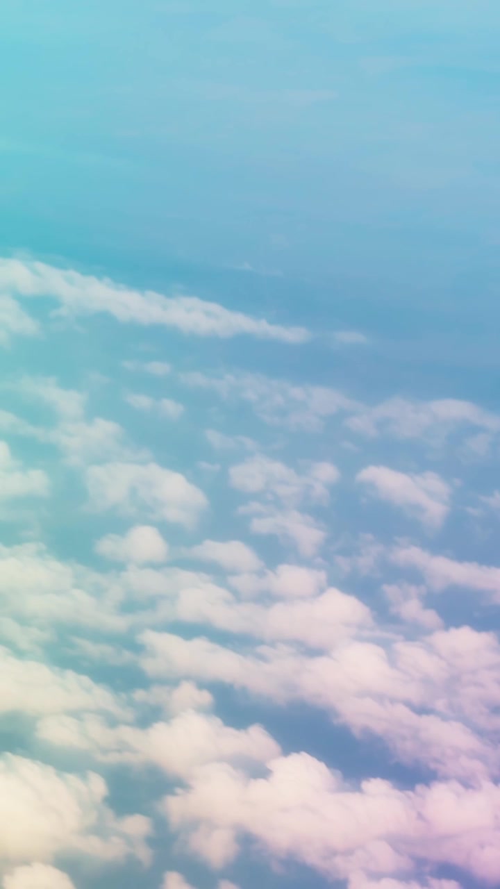 Vertical aerial view of soft clouds beneath a pale blue sky, creating a calm high-altitude atmosphere with dreamy light and a minimal travel background.