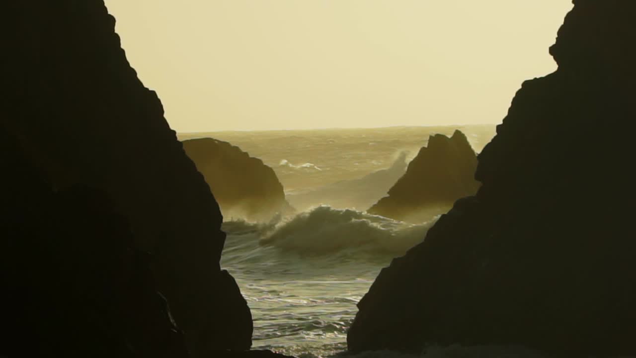 Full shot, Ocean waves hitting Rock formation on the Ursa beach in Lisbon, Portugal, Sun light in the background