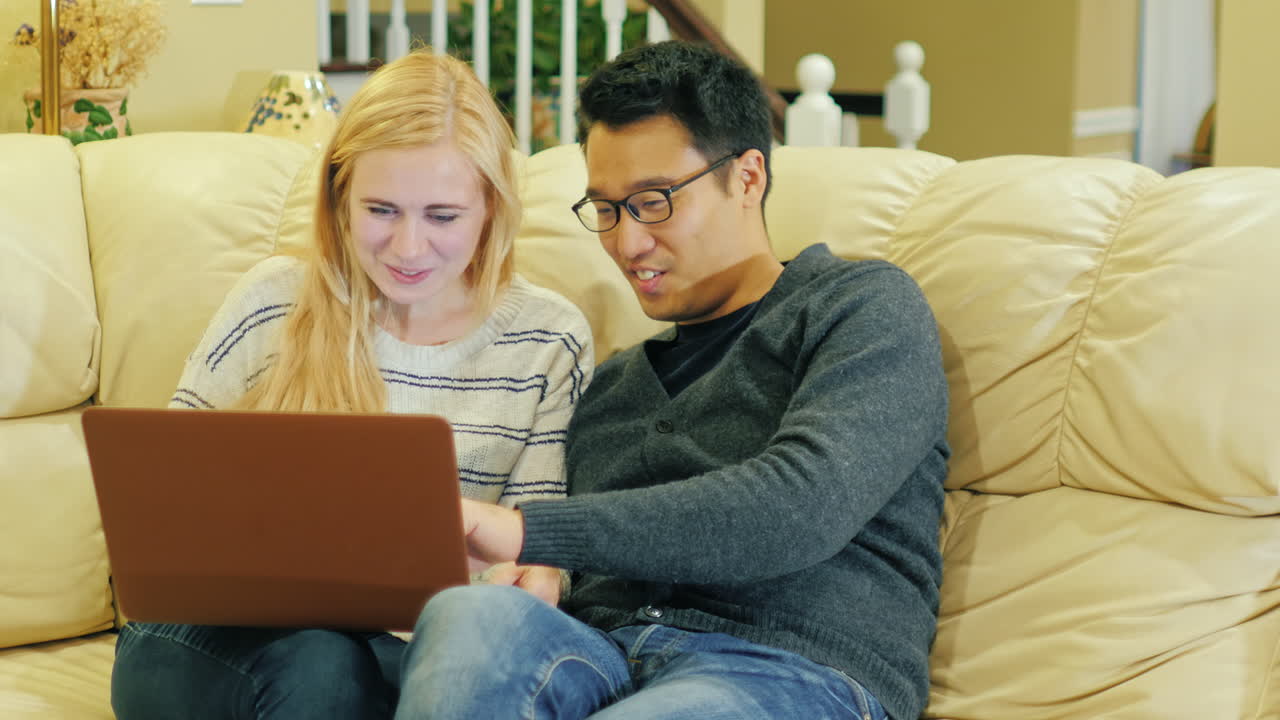 una pareja joven sentada en el sofá usando una computadora portátil 1