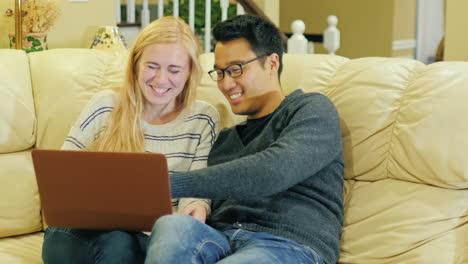 una pareja joven sentada en el sofá usando una computadora portátil 1