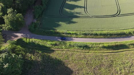 A-blue-jaguar-car-driving-next-to-a-farm-aerial-view