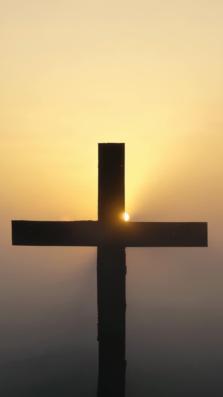 Vertical video: Rising sun tracking along wooden cross at misty hilltop, backlighting silhouette