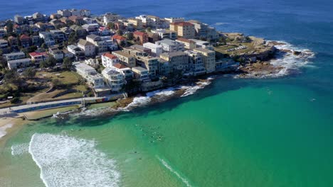 Luftaufnahme-Von-Hotelgebäuden-In-Ben-Buckler-Point-Mit-Surfern,-Die-Im-Blauen-Meer-Schwimmen