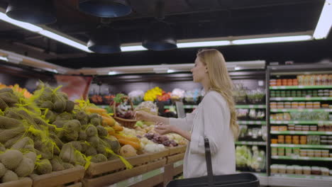 at the supermarket: beautiful young woman walks through fresh produce section chooses vegetables and puts them in her shopping cart