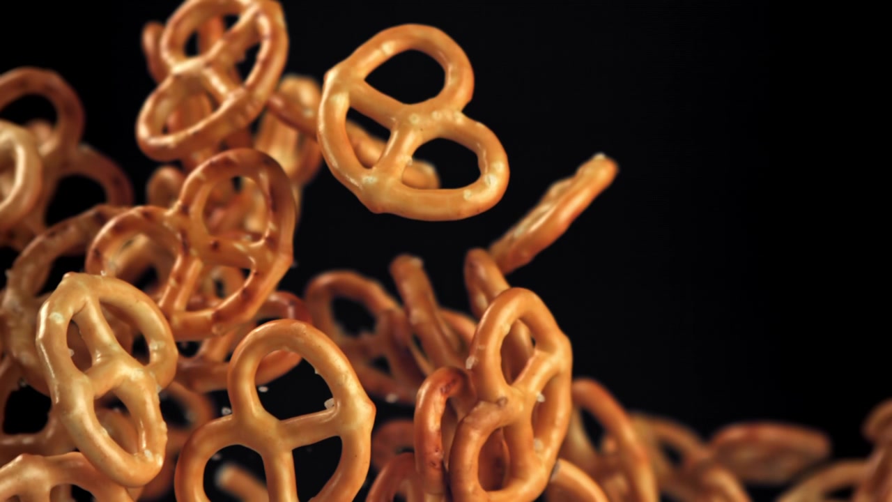 Pretzel dorati che cadono al rallentatore su uno sfondo nero.