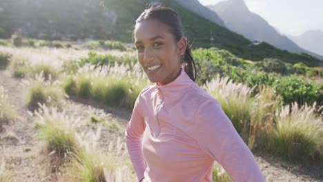 Portrait-of-smiling-mixed-race-woman-exercising-resting-during-a-run-in-countryside