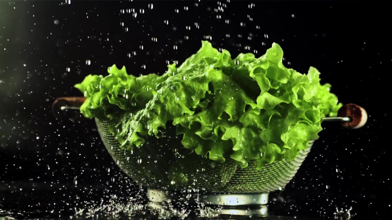Slow motion opname van water dat verse groene sla wast