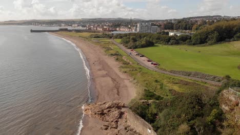 Aerial-view-of-sandy-beach-with-car-park-to-the-right-and-harbour-in-the-distance