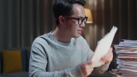 close up of happy asian man celebrating finishing working with documents at home