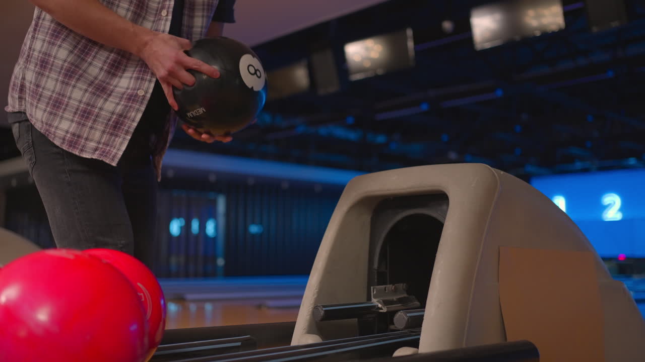 A man in a bowling club picks up a black bowling ball with the number 8 in slow motion. Preparation for a throw in bowling