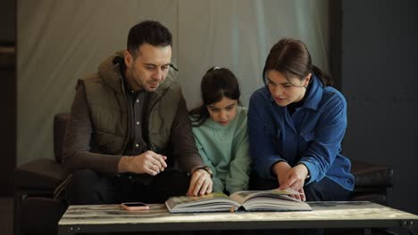a husband wife and their daughter look through a catalog while sitting in a furniture showroom a husband wife and their daughter look through a catalog while sitting in a furniture showroom selection of furniture for the home