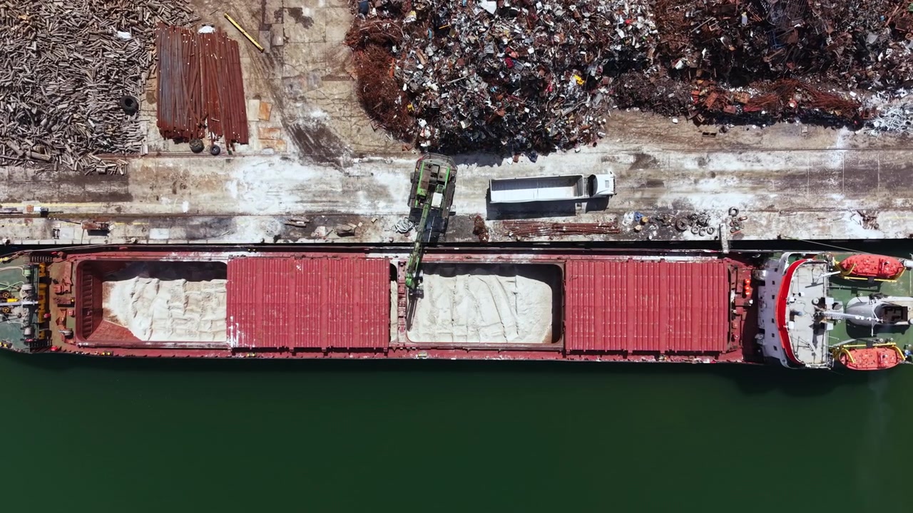 Nave da carico in porto che scarica materiali mentre gli operai portuali gestiscono le attrezzature in una trafficata area di spedizione.