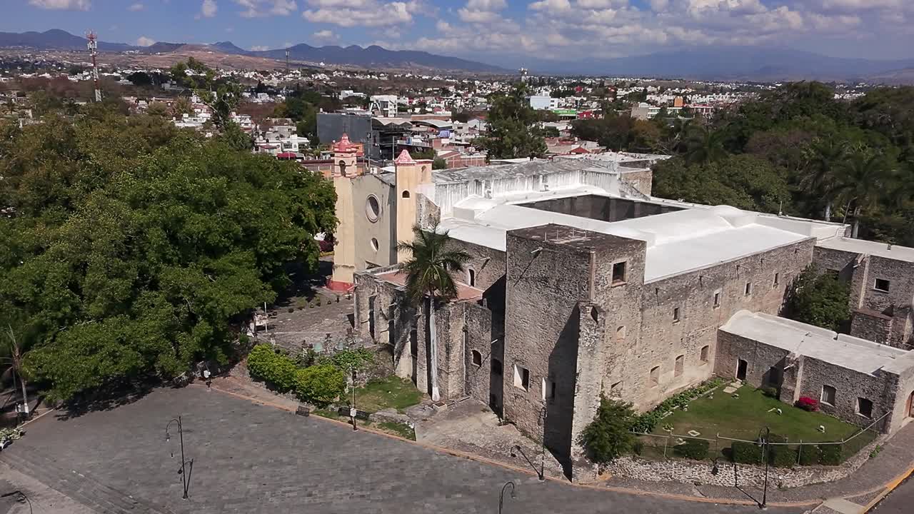 Aerial: old building in Oaxtepec during the day with cityscape and blue sky in Morelos, Mexico, establishing drone shot