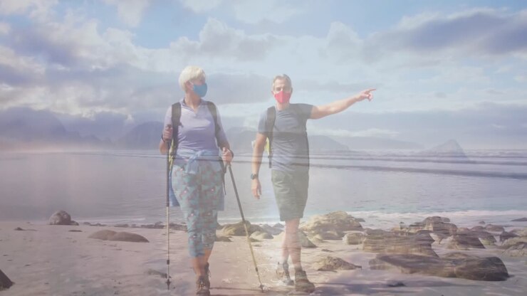 Caucasian senior couple in face masks hiking on the coast, over moving sea