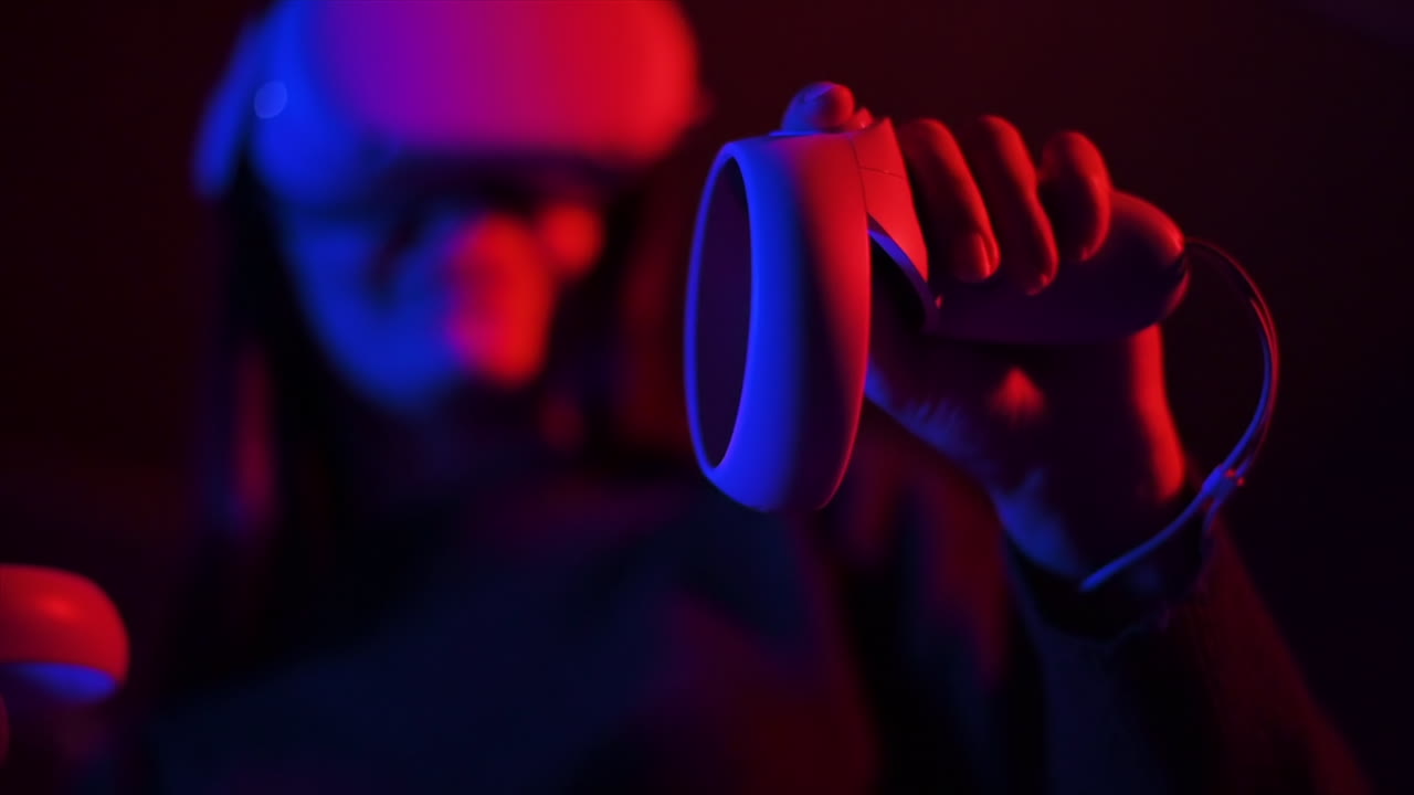 A young woman holding controllers while wearing VR glasses, Red and blue illumination. Slow motion