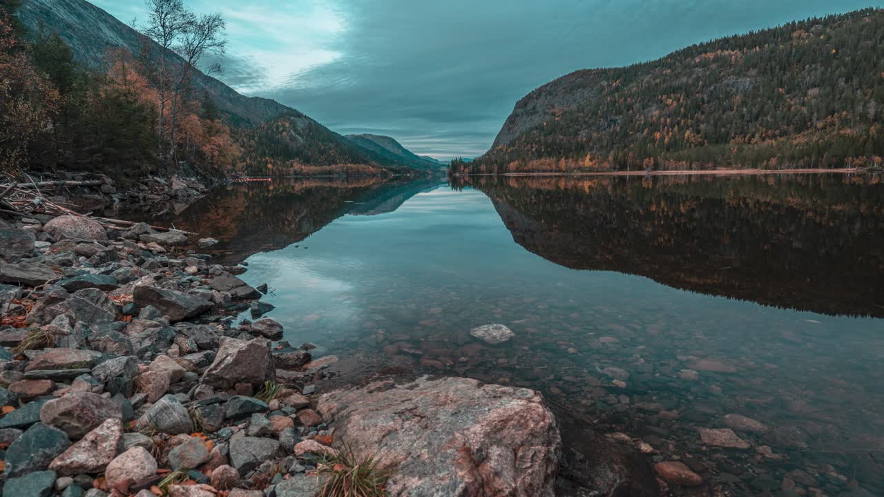 Dark autumn clouds and forest-covered hills are reflected in the still mirrorlike surface of the mountain lake