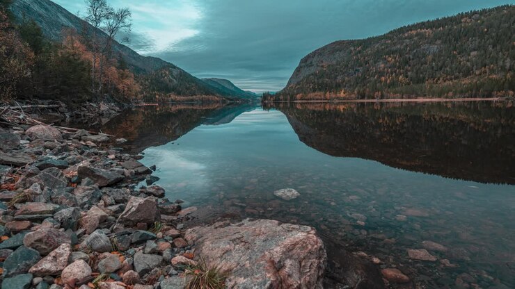 Nuvole autunnali scure e colline coperte di foreste si riflettono sulla superficie immobile e specchiante del lago di montagna
