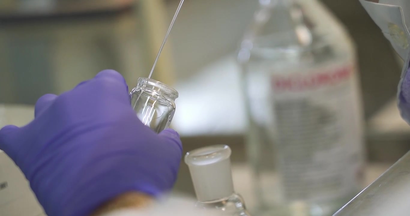 Scientist with purple surgical gloves adding serum to a bottle ; close-up