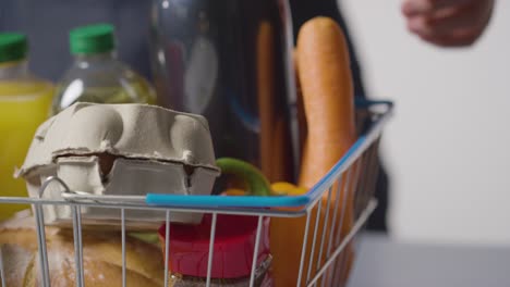 close up of person unpacking basic food items from supermarket wire shopping basket