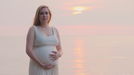 a pregnant woman is standing near the sea at the back of her bed stroking her belly