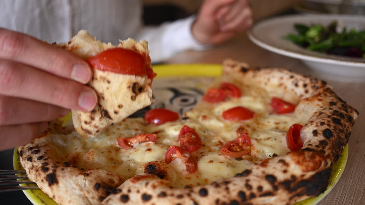 Mano che solleva una fetta di pizza al formaggio appena sfornata e condita con pomodorini.