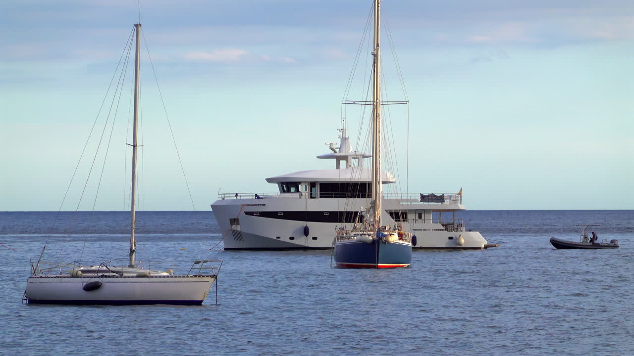 Barche a vela e un moderno yacht a motore ancorati nelle calme acque blu del Mar Mediterraneo