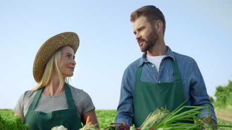 Portrait-Shot-Of-The-Good-Looking-And-Happy-Woman-And-Man-Farmers-Smiling-To-The-Camera-On-The-Field-With-Harvested-Vegetables-In-Hands