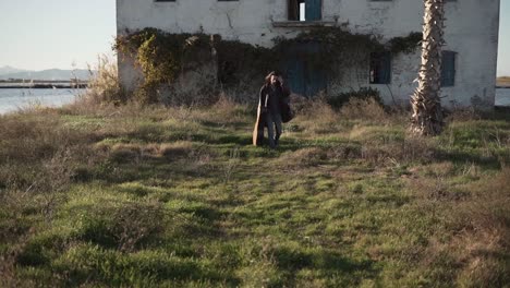 man with guitar walking in abandoned farmhouse field