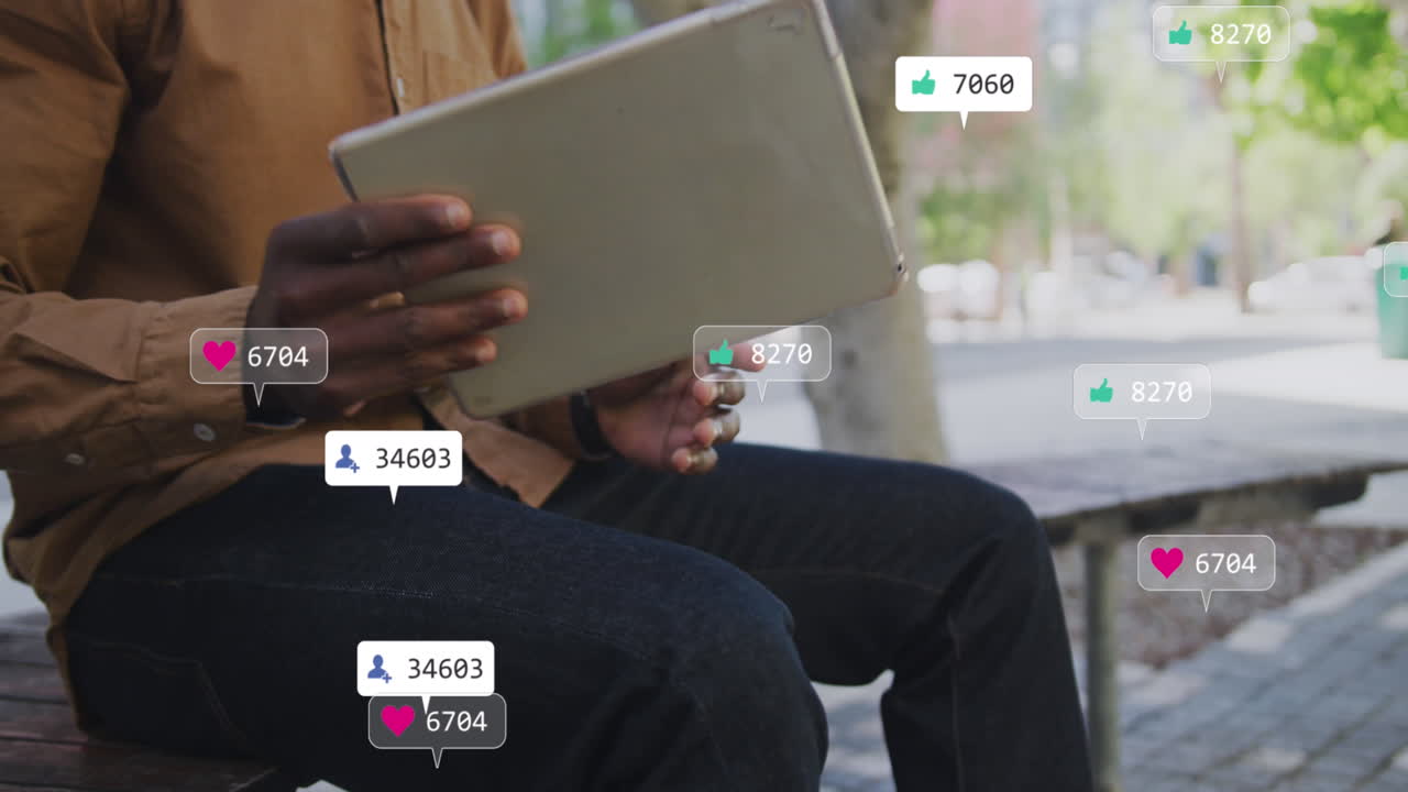 Animation of social media icons over mid section of man using tablet sitting on bench on the street