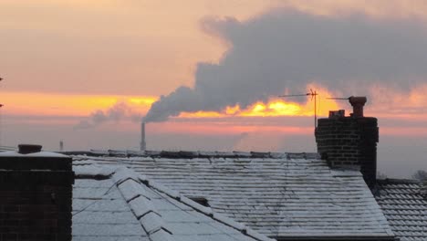 smoking industry chimney above frosty wintery home rooftops glowing sunrise orange sky