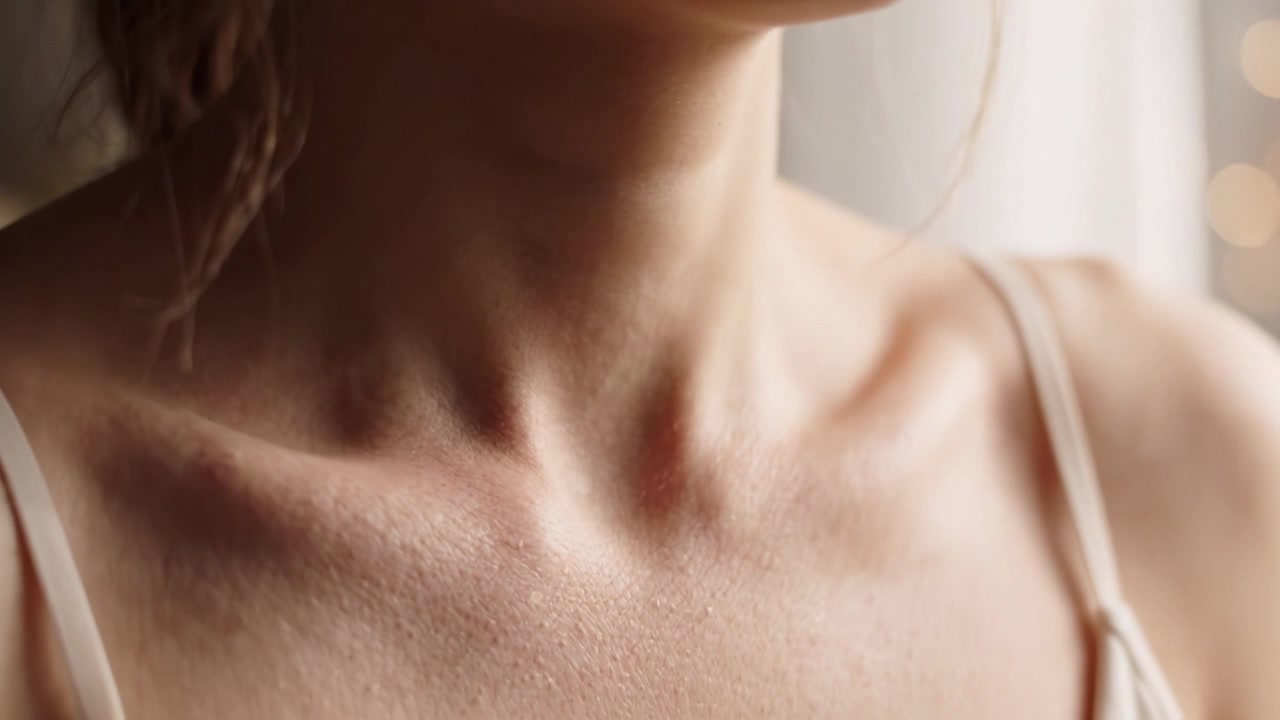 Primo piano intimo della zona del collo e della clavicola di una persona, che mostra la texture naturale della pelle e delicati effetti di luce in un ambiente interno sereno