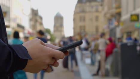 Schwenkaufnahme-Eines-Mannes,-Der-In-Einer-Belebten-Straße-SMS-Auf-Dem-Handy-Schreibt