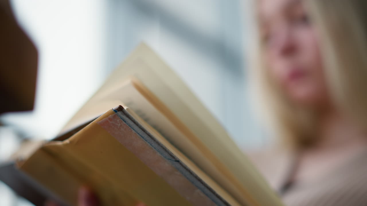 primer plano de una mujer con ropa tejida intentando pasar a la siguiente página de un libro con un ligero borrón del fondo, la textura suave de su suéter contrasta con la claridad del libro