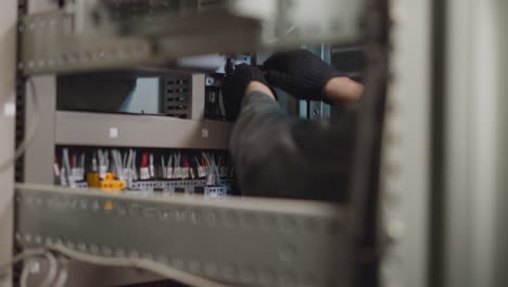 electrician uses screwdriver to tighten nut in power cabinet