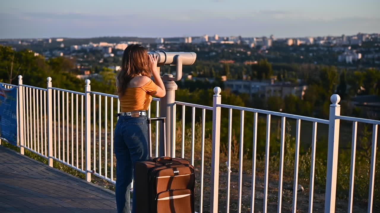 Giovane donna con mascherina medica protettiva che guarda attraverso un binocolo a colonna dalla terrazza panoramica della città al tramonto. Idea sul Coronavirus. Viaggiare sicuri durante la pandemia. Rallentatore. Chișinău, Moldavia