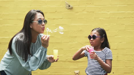 biracial mother and daughter in sunglasses blowing bubbles