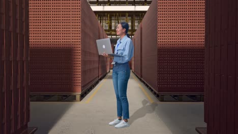full body side view of asian female with red brick packed in stacks are stored, observes by looking up before she come to concentrating on the laptop and keep on typing