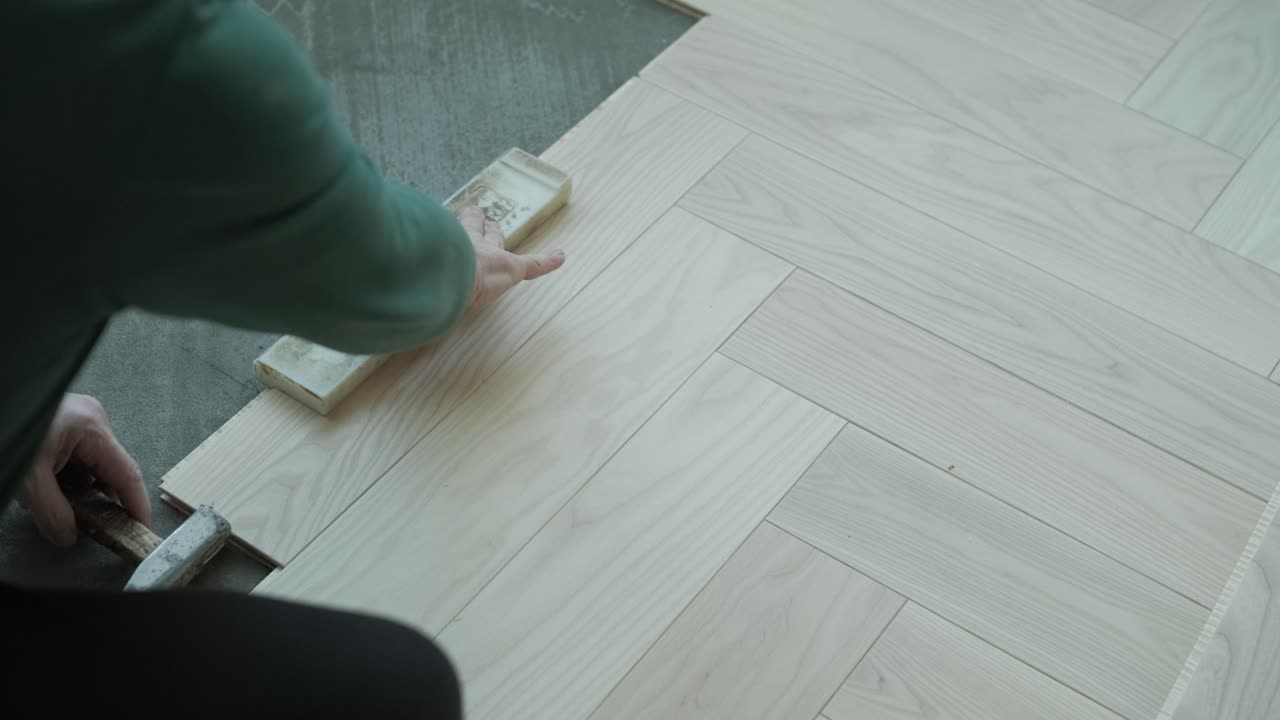 Worker installing wooden flooring with hammer and tapping block