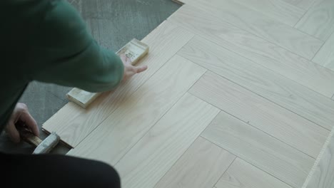worker installing wooden flooring with hammer and tapping block