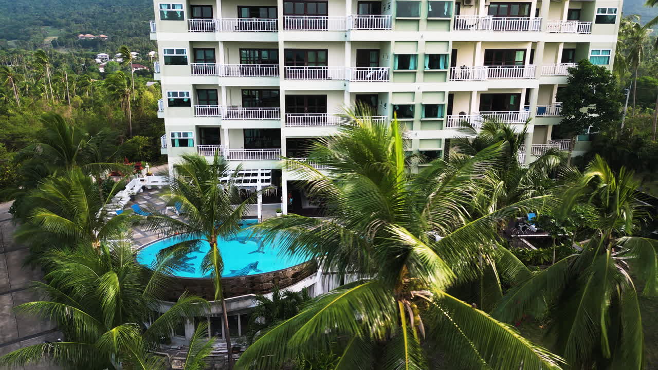 Hotel tropical de lujo con palmeras y piscina, vista aérea en órbita.